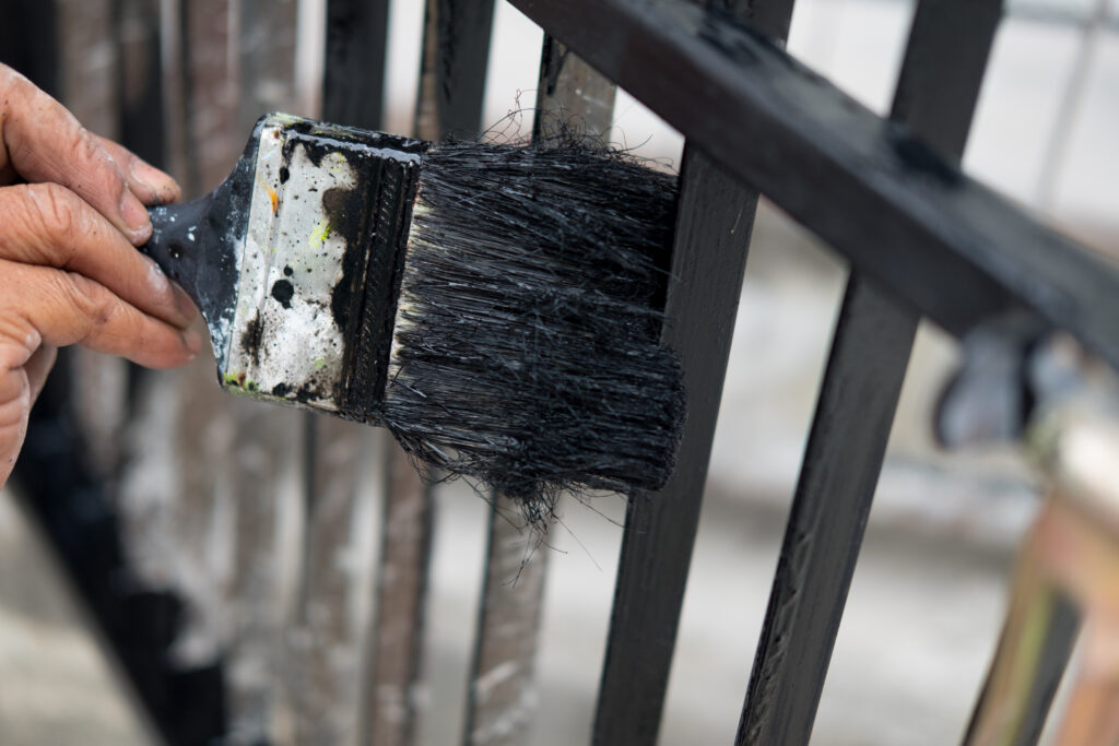 Painting Your Fence Hand with paintbrush painting iron fence with black paint. Concept of renovation house