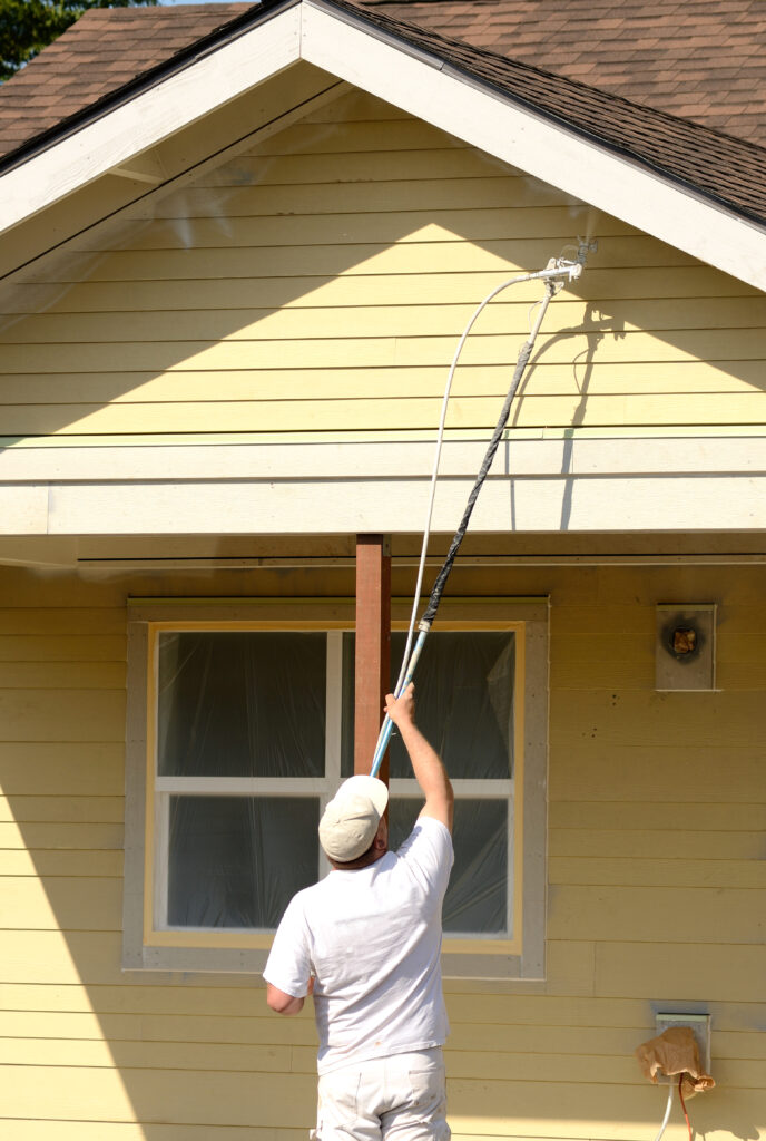 A painting contractor uses a extension on his spray gun to paint a overhang on a commercial residential development. Staining Wood