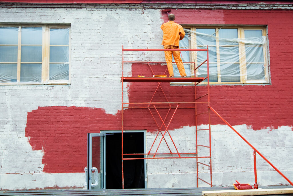 Man painting a brick wall in red Staining Wood