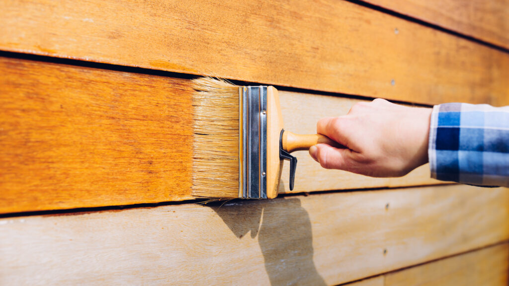Female hand painting wooden wall with a brush - painting woodwork outside Staining Wood
