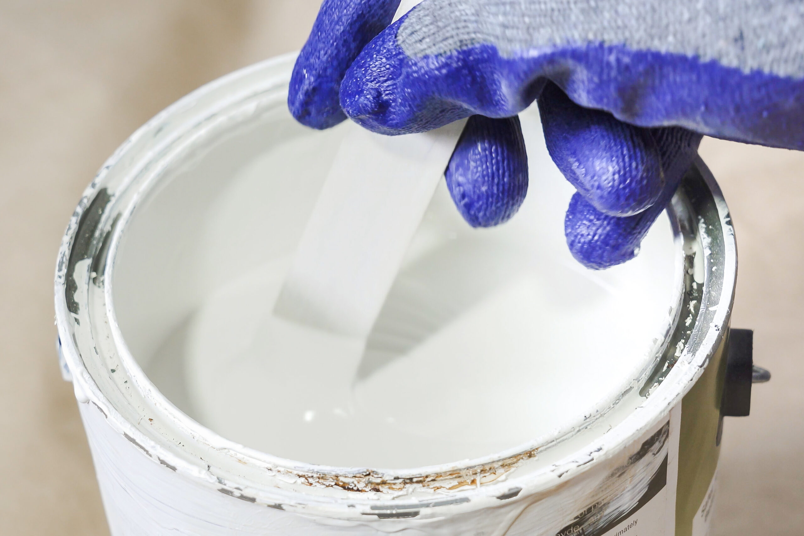 Close up of hand gloved painter mixing paint in metal paint can with wooden stick. composition of paint